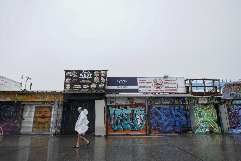 A person walks past closed vendor stands at Venice Beach, Sunday, Aug. 20, 2023, in Los Angeles. Tropical Storm Hilary swirled northward Sunday just off the coast of Mexico's Baja California peninsula, no longer a hurricane but still carrying so much rain that forecasters said "catastrophic and life-threatening" flooding is likely across a broad region of the southwestern U.S. (AP Photo/Ryan Sun)