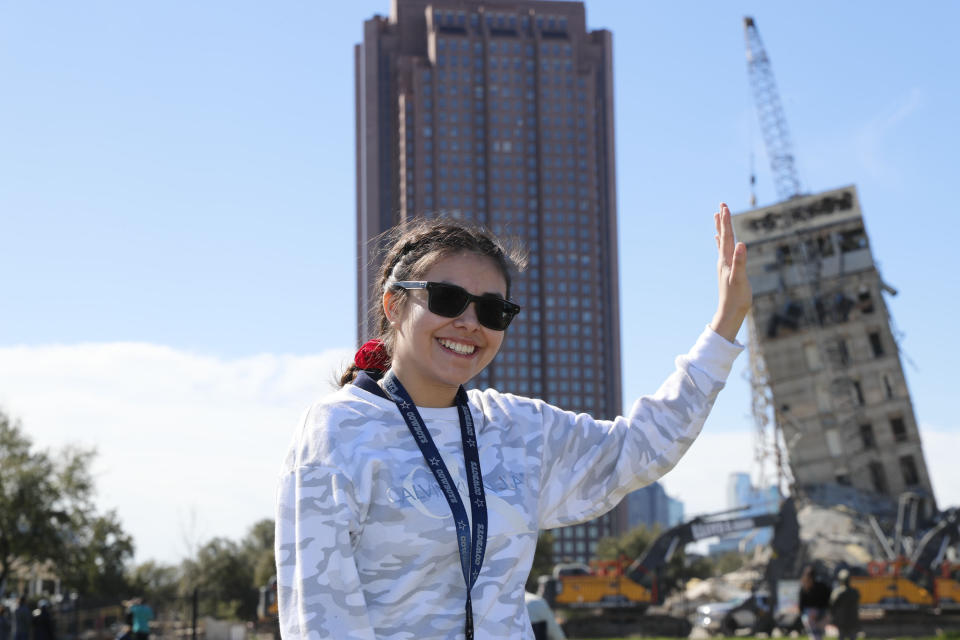 Eloisa Alvarado poses for a photo as she and friends watch the demolition of the so called "Leaning Tower of Dallas" as a wrecking ball works to topple the structure north of downtown Dallas, Monday, Feb. 24, 2020. The still standing structure is part of an 11-story building that found a second life online after surviving a first demolition attempt. The former Affiliated Computer Services building inspired jokes and comparisons to Italy's Leaning Tower of Pisa when a Feb. 16 implosion failed to bring down its core. The company that engineered the blast said some explosives did not go off. (AP Photo/LM Otero)