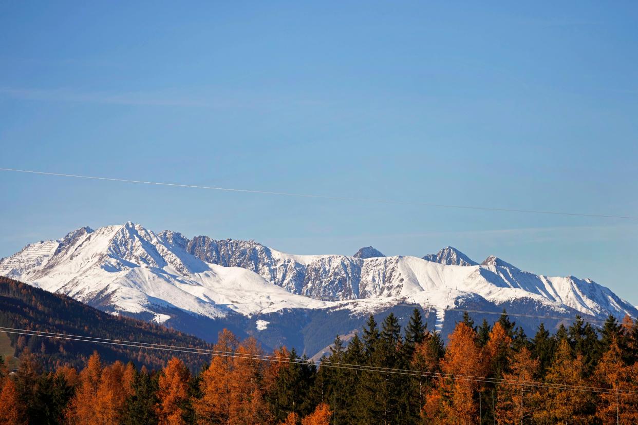 Snow covers the Alps mountains behind autumn colorful trees near Innsbruck, Austria, Saturday, Nov. 20, 2021