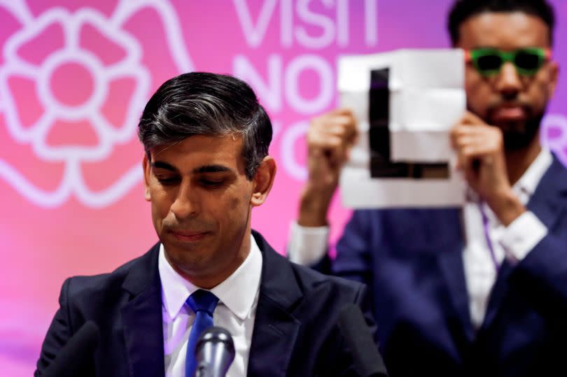 Niko Omilana holds an "L" as former Prime Minister Rishi Sunak speaks