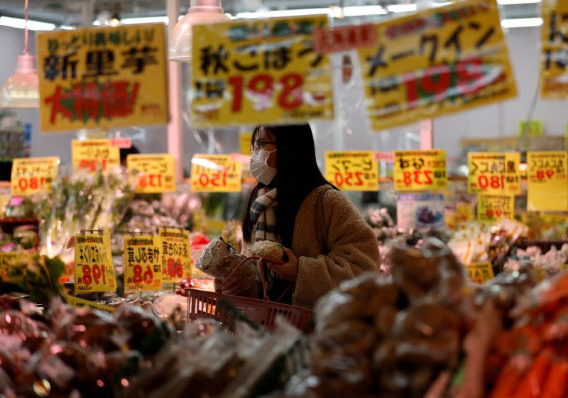 FILE PHOTO: A shopper is reflected on a mirror glass as she checks food items at a supermarket in Tokyo