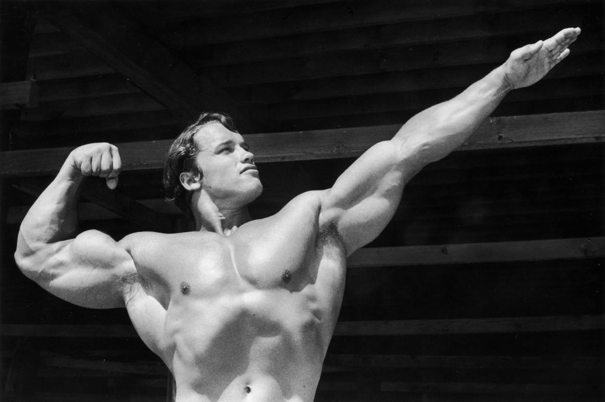 circa 1966: Austrian-born bodybuilder Arnold Schwarzenegger points one hand out as he flexes his torso on Muscle Beach, Santa Monica, California.
