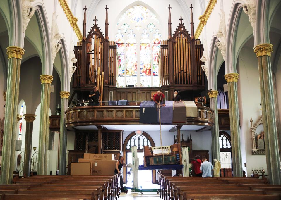 Danny Allen, top center, holds a strap as Shan Fultz, bottom left, and Octavius Hayes, bottom right in red, all of D.C. Moore & Son Inc. from Sanford, crank a hand lift to lower an old organ console that is being replaced at the Basilica of The Immaculate Conception.