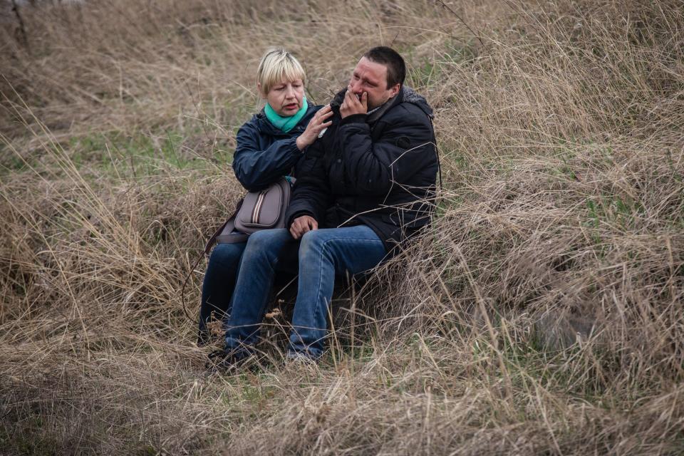 A woman and a man sit on a grassy hill, comforting one another.