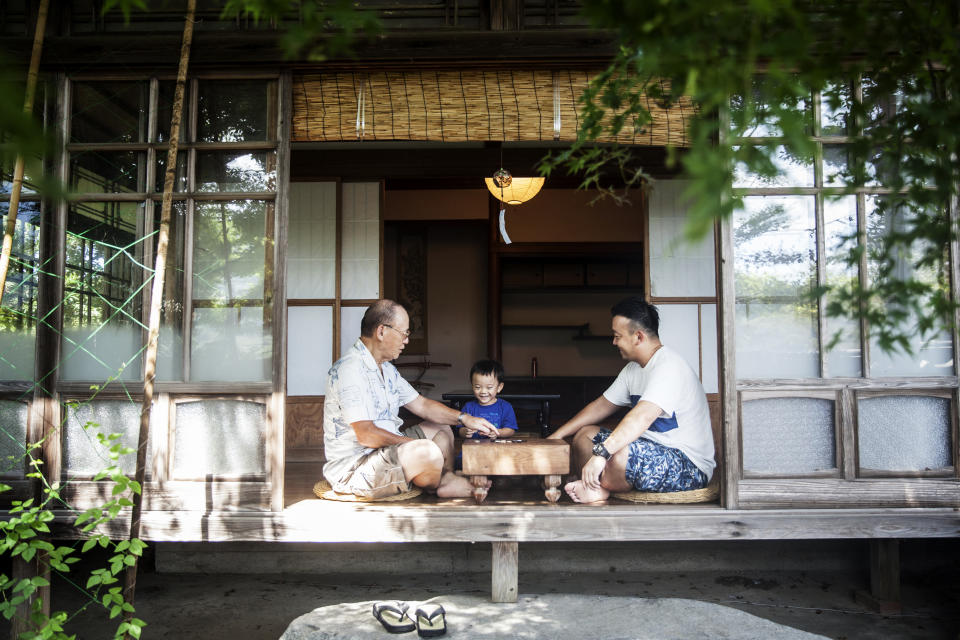 Two Japanese men and little boy sitting on floor on porch of traditional Japanese house, playing Go.