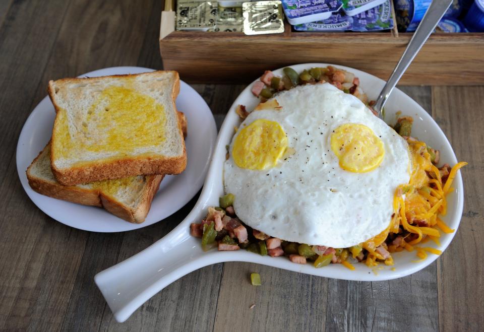 A Western breakfast skillet with breakfast potatoes, bacon, ham, green peppers and onions is topped with cheddar cheese and two eggs and accompanied by buttered toast at Frankie's Restaurant on Wednesday, Aug. 16, 2023.