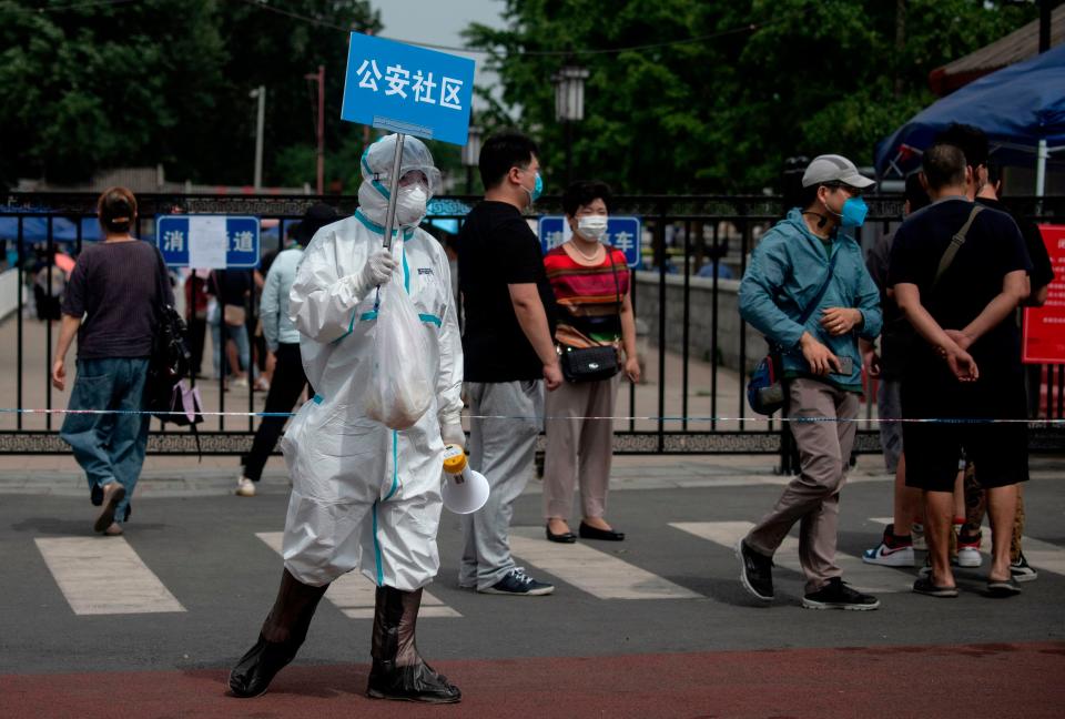 A medical worker in full protective gear holds up a sign to assist people who live near or who have visited the Xinfadi Market, a wholesale food market where a new COVID-19 coronavirus cluster has emerged, as they arrive for testing in Beijing on June 17, 2020.