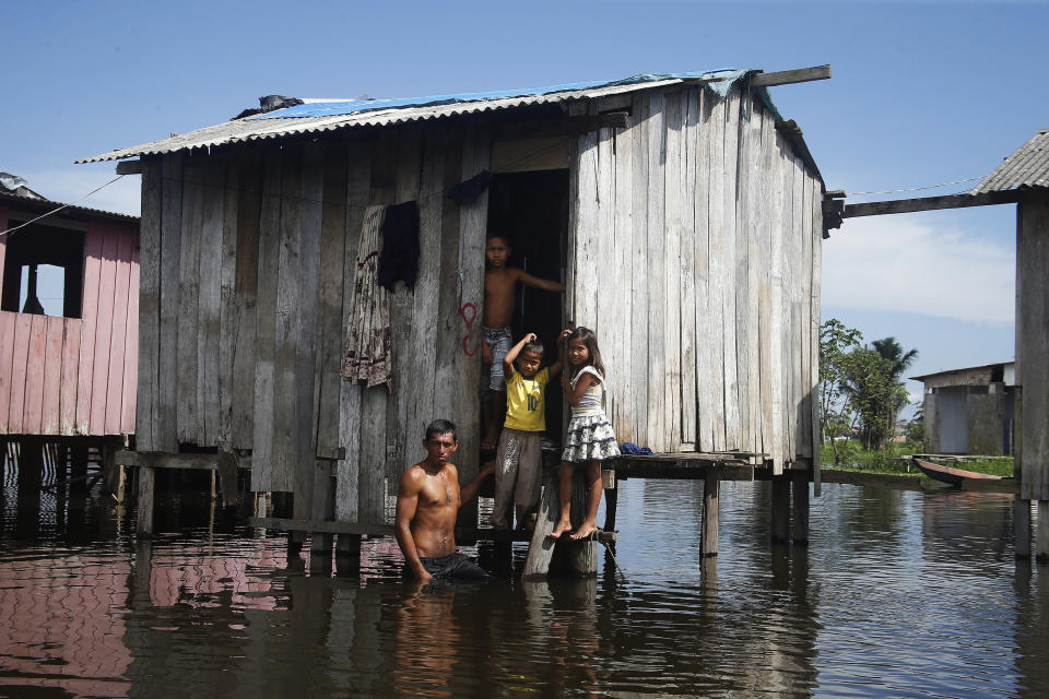 Francisco Fabiano Rodrigues and his children stand on the porch of their home on a street flooded by the rise of the Negro river in Iranduba, Amazonas state, Brazil, Monday, May 23, 2022. The Amazon region is being hit hard by flooding with 35 municipalities that are facing one of their worst floods in years and the water level is expected to rise over the coming months. (AP Photo/Edmar Barros)