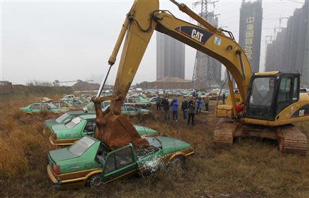 Photographers take pictures of old taxis being scrapped by a Caterpillar excavator in Changsha, Hunan province, in this December 17, 2012 file photo. REUTERS/Stringer/Files