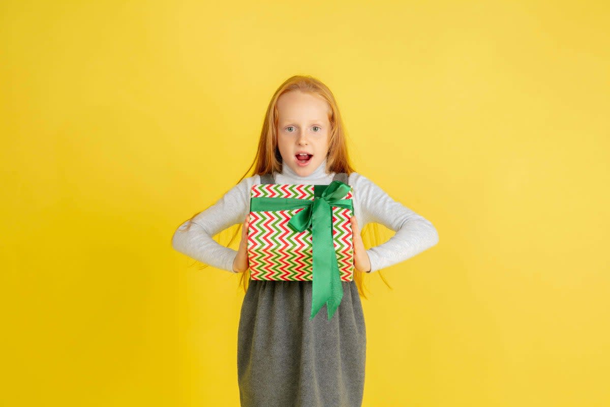 2D9EMGG Giving and getting presents on Christmas holidays. Teen smiling girl having fun, holding big gifts isolated on yellow studio background. New Year 2021 meeting, childhood, happiness, emotions.