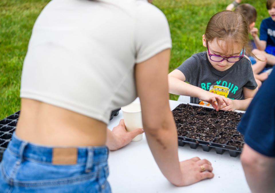 Grandview Elementary student Paislee Moore is helped by Andrea Florez, a volunteer with Ivy Tech Community College, to distribute seeds into starter cups at the college's Biology Outdoor Learning Lab on Tuesday, May 10, 2022.