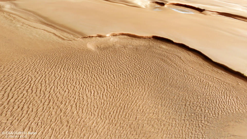 nearly ground-level view of rippling martian sand dunes, with some ice-covered escarpments in the distance