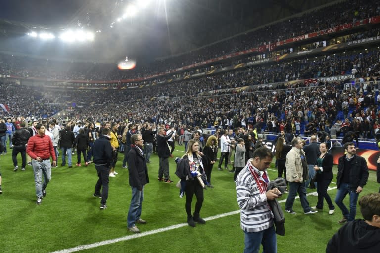 People stand on the pitch as Besiktas and Lyon fans fight before their UEFA Europa League first leg quarter final match on April 13, 2017, at the Parc Olympique Lyonnais stadium in Decines-Charpieu, central-eastern France