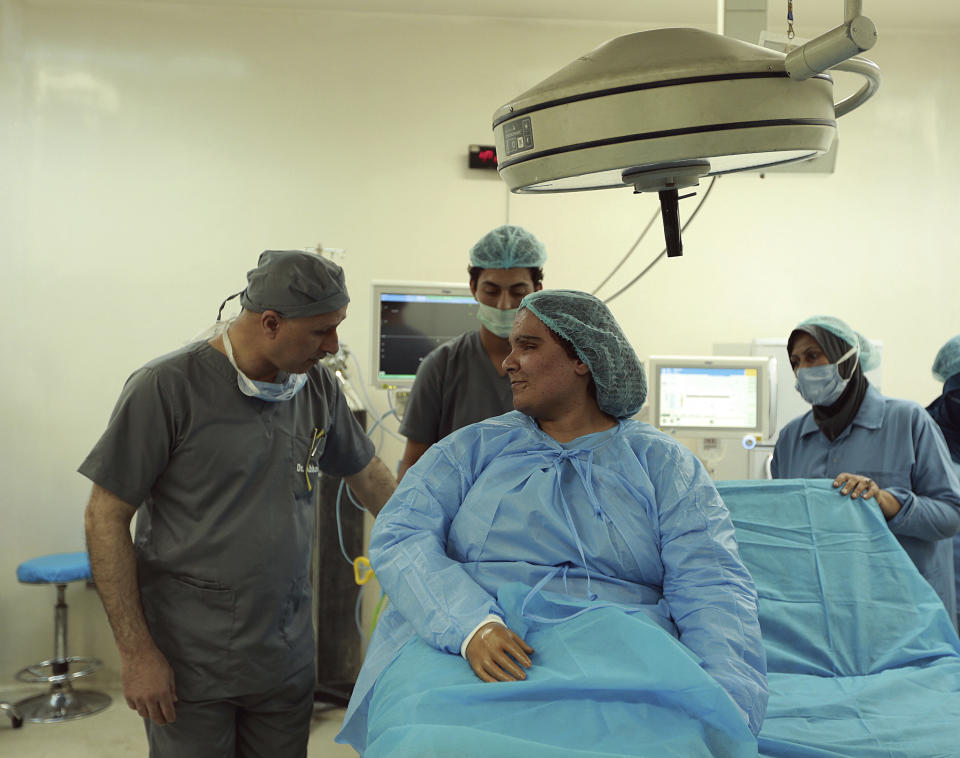 In this Tuesday, Nov. 6, 2018 photo, plastic surgeon Dr. Abbas al-Sahan, left, talks to Saja Ahmed Saleem, who was injured in an explosion in 2007, before her reconstructive surgery in Baghdad, Iraq. Those whom treatment not available at state-run hospitals and can’t afford treatment at private clinics rely on social media to make appeals that grab attention of some surgeons to help them regain a chance at life. (AP Photo/Hadi Mizban)