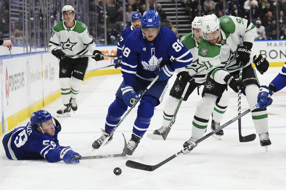 Toronto Maple Leafs forward Tyler Bertuzzi (59) reaches for the puck, as do forward William Nylander (88) and Dallas Stars forward Tyler Seguin (91) during the second period of an NHL hockey game Wednesday, Feb. 7, 2024, in Toronto. (Nathan Denette/The Canadian Press via AP)