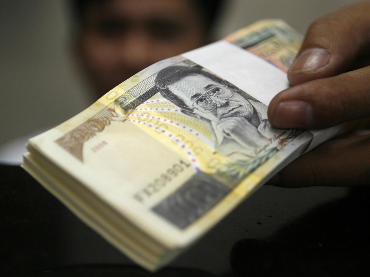 FILE PHOTO: An employee hands out a bundle of peso bills to a customer who exchanges with dollars at a money changer in Manila, Philippines. REUTERS/Cheryl Ravelo