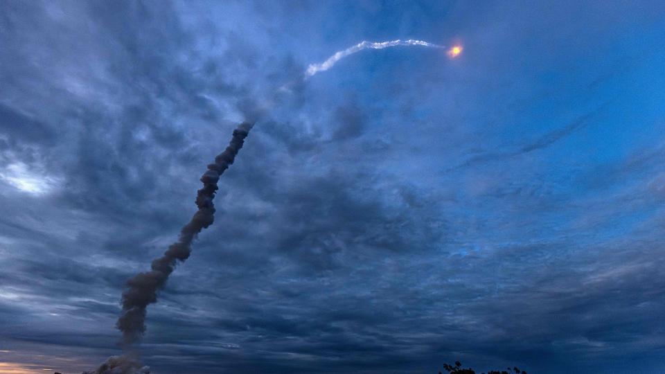 a rocket can be seen in the distant sky above a long trail of smoke