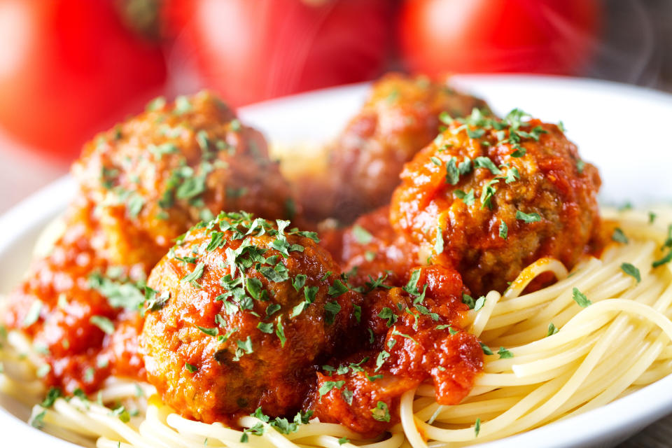 A close-up of a plate of spaghetti topped with four meatballs, marinara sauce, and garnished with chopped herbs