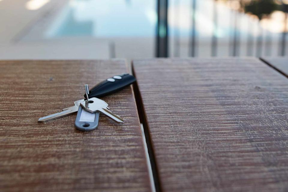 <p>Getty</p> House keys on wooden table against swimming pool