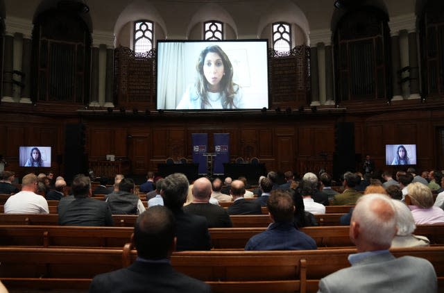 Suella Braverman on a big screen as people sitting on pews watch her