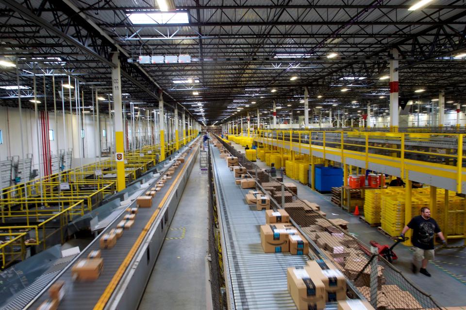 A view of Amazon boxes going down a conveyor belt in a large warehouse space.