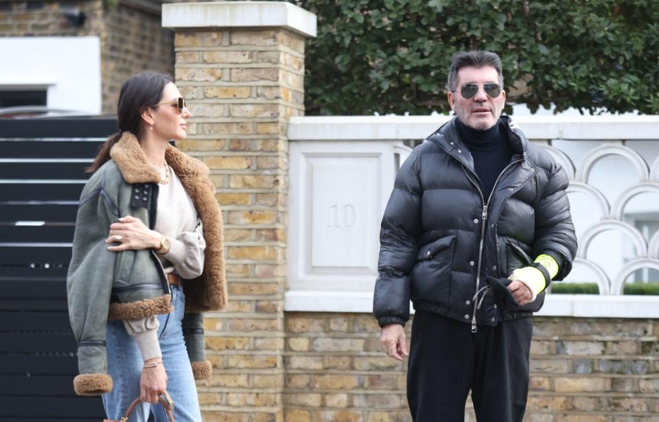 Simon Cowell shows the broken arm he suffered following a bicycle injury as he and his partner Lauren Silverman leave their home in London's Holland Park. (PA)