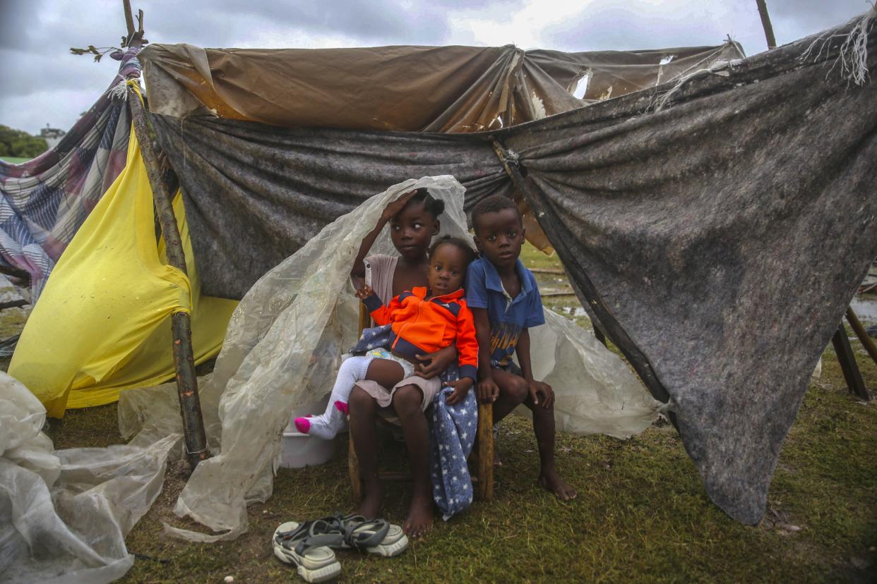 Earthquake-displaced children huddle under a piece of plastic the morning after Tropical Storm Grace swept over Les Cayes, Haiti, Tuesday, Aug. 17, 2021, three days after a 7.2-magnitude earthquake.