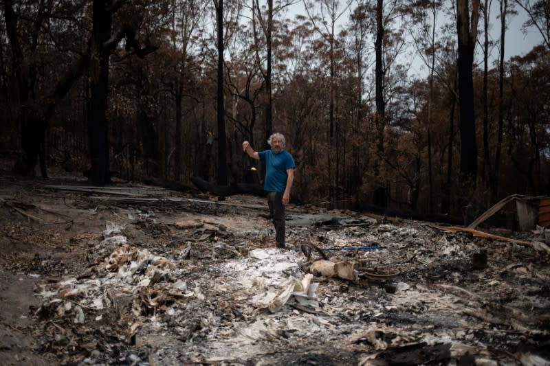 Australian surfer David Ford stands over the remains of a burnt shed where he kept his vintage surfboard collection that was destroyed in the recent bushfires in Lake Conjola