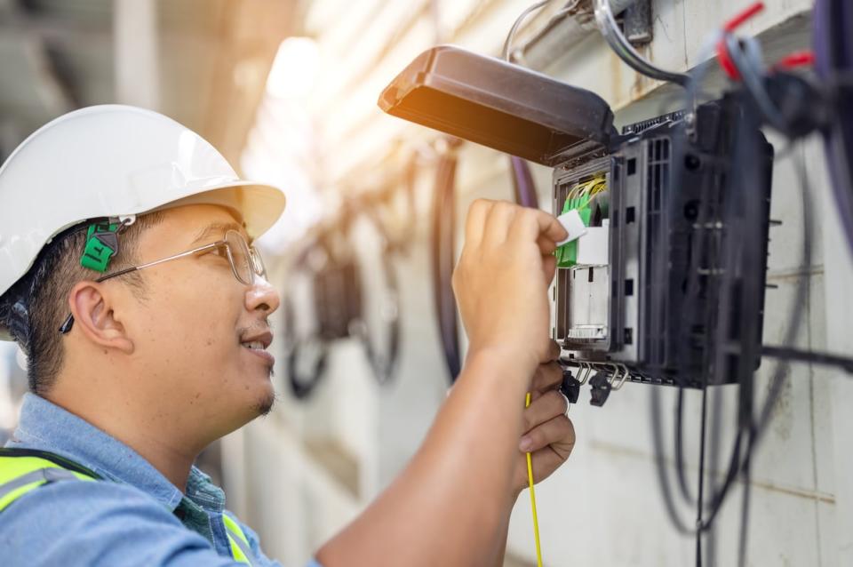 A person smiles while  wearing personal protective equipment and working with electronics. 