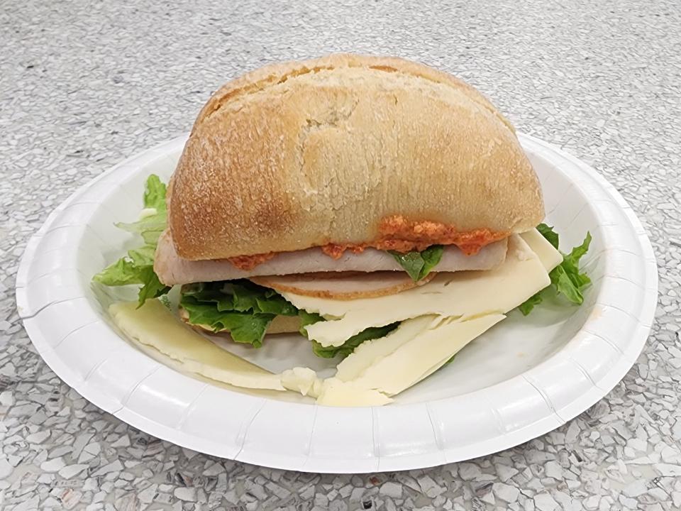 A turkey sandwich on ciabatta with cheese and lettuce sits on a paper plate on a gray counter