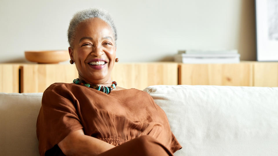 A woman with grey hair wearing a brown dress sitting on a couch