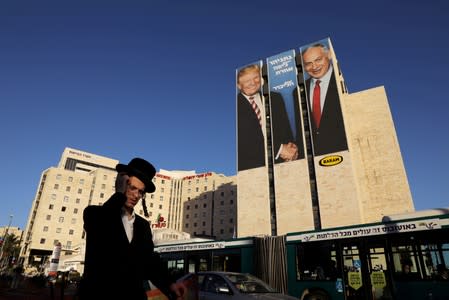 FILE PHOTO: A man walks past a Likud election campaign billboard depicting U.S. President Trump shaking hands with Israeli PM Netanyahu, in Jerusalem