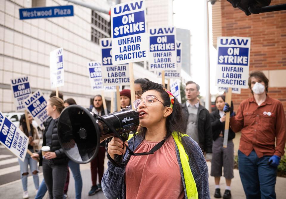 Students hold signs that say "UAW On Strike Unfair Labor Practice"