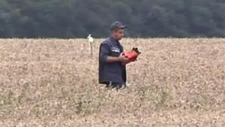 A rescue worker walks across a field carrying a flight data recorder at the crash site of Malaysia Airlines Flight MH17 in Hrabove July 18, 2014 in this still image taken from video. REUTERS/Reuters TV