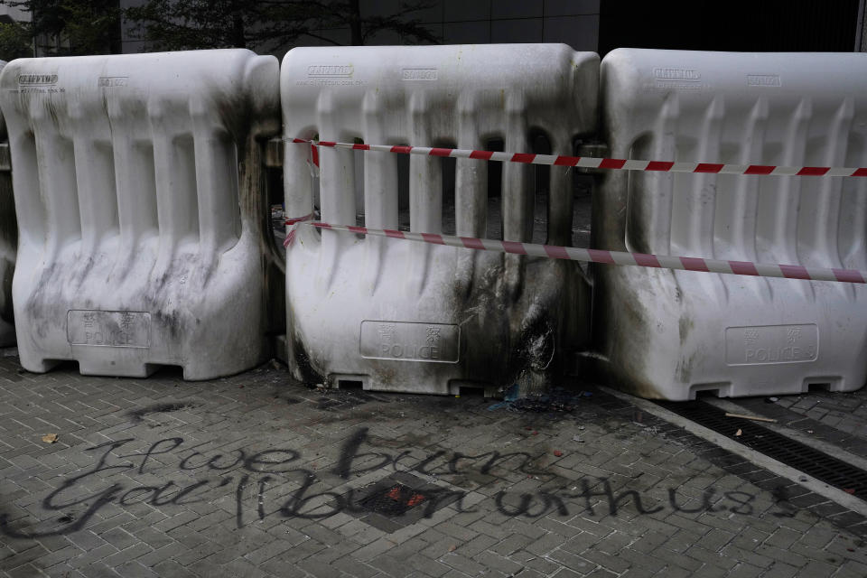 In this Sept. 16, 2019, photo, an ominous quote "If we burn, you'll burn with us" from the movie "Hunger Games: Mockingjay" is scribbled in front of plastic barriers which are burned after protesters threw Molotov cocktail in front of government head quarters in Hong Kong. As Hong Kong enters its fourth month of steady protests, the city is embracing for another violent weekend prior to the upcoming 70th National Day on Oct. 1. (AP Photo/ Vincent Yu)
