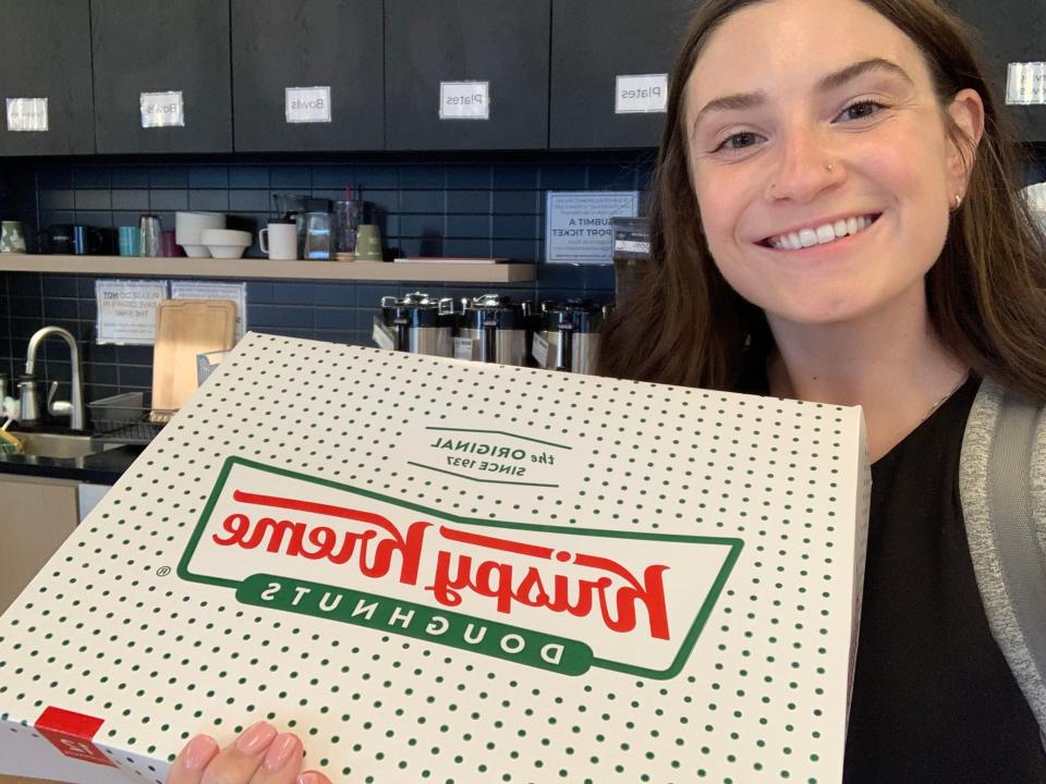 The author, smiling, holds a box of a dozen donuts from Krispy Kreme.