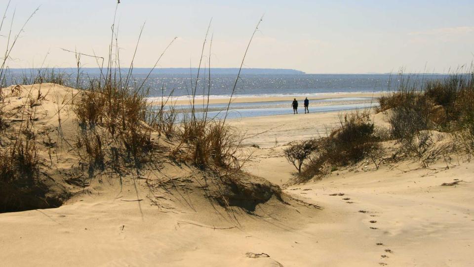 View through the dunes to two people walking on the beach at Jekyll Island, Georgia