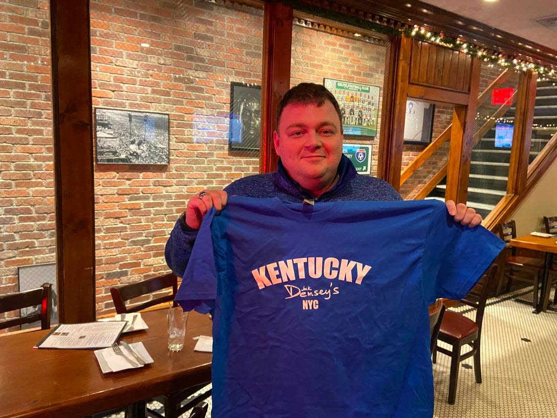 New York City UK Alumni Club President Zebulon “Zeb” Vance is shown holding a blue and white Kentucky shirt that also features the logo of Jack Demsey’s. The bar and restaurant is the gathering spot for the Kentucky Alumni Supporter’s Club in New York City.