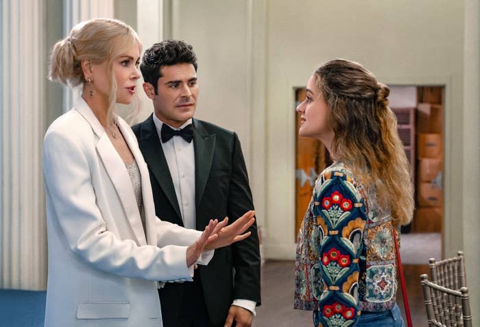 Nicole Kidman in a blazer, Zac Efron in a tuxedo, and Joey King in a colorful patterned jacket are engaged in a conversation