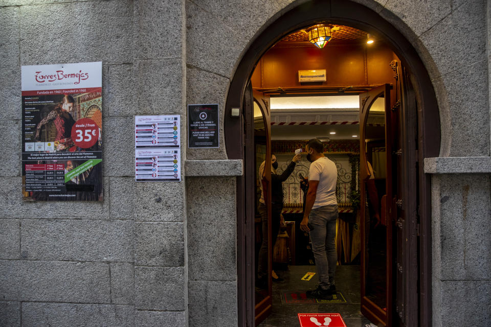 A staff worker checks a customer's body temperature before he enters at the Torres Bermejas "tablao," or live flamenco venue, in Madrid, Spain, Saturday, Sept. 26, 2020. The passion and drama of live flamenco shows are back on stage in Madrid. But now the performers are behind Perspex screens and keeping their distance from the audience. The Torres Bermejas “tablao,” or live flamenco venue, has reopened its doors to customers after seven months closed due to the COVID-19 pandemic. (AP Photo/Manu Fernandez)