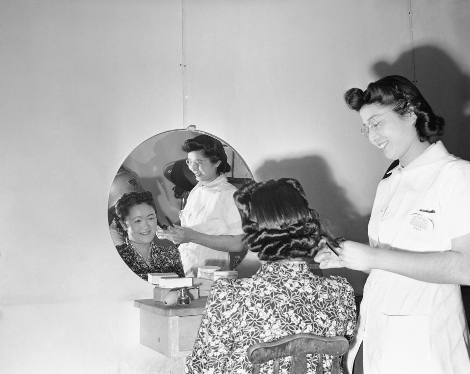 FILE - In this May 23, 1943, file photo, Mary Takita of Walnut Grove, Ca, works on the hair of Mrs. Y. Yoshihara of Olympia at the Japanese relocation camp in Tule Lake, Calif., May 23, 1943. As the 75th anniversary of the formal Sept. 2 surrender ceremony that ended WWII approaches, Hidekazu Tamura, a former Japanese-American living in California, has vivid memories of the wartime years he spent in the United States, torn between two nationalities, and the events that led him to renounce his American citizenship and return to Japan. During the pacific war period, Tamura was at Tule Lake, a segregation center for those deemed disloyal, where he joined a group called “Hokoku Seinen Dan,” which means, “Young Men’s Association to Serve the Fatherland.” (AP Photo, File)