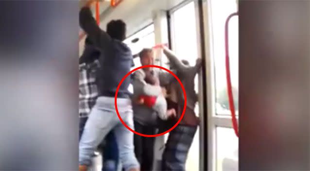 The woman is pushed and shoved while still holding her young child.