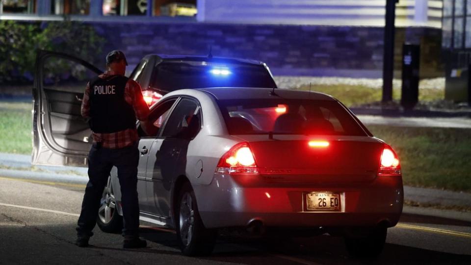 Police car with brake lights on, officer in vest that says "Police".