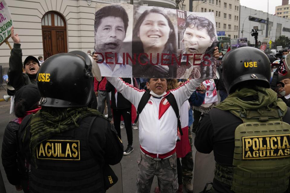 An opponent of the government of President Pedro Castillo holds photos of Castillo, his sister-in-law Yenifer and his wife Lilia Paredes with text that reads Spanish, "Criminals," gather outside a court building to protest against Yenifer Paredes, the sister-in-law of President Castillo, in Lima, Peru, Sunday, Aug. 28, 2022. A judge will decide if Paredes should be held in preventive detention for 36 months, as requested by the prosecution for her alleged participation in a corruption network. (AP Photo/Martin Mejia)