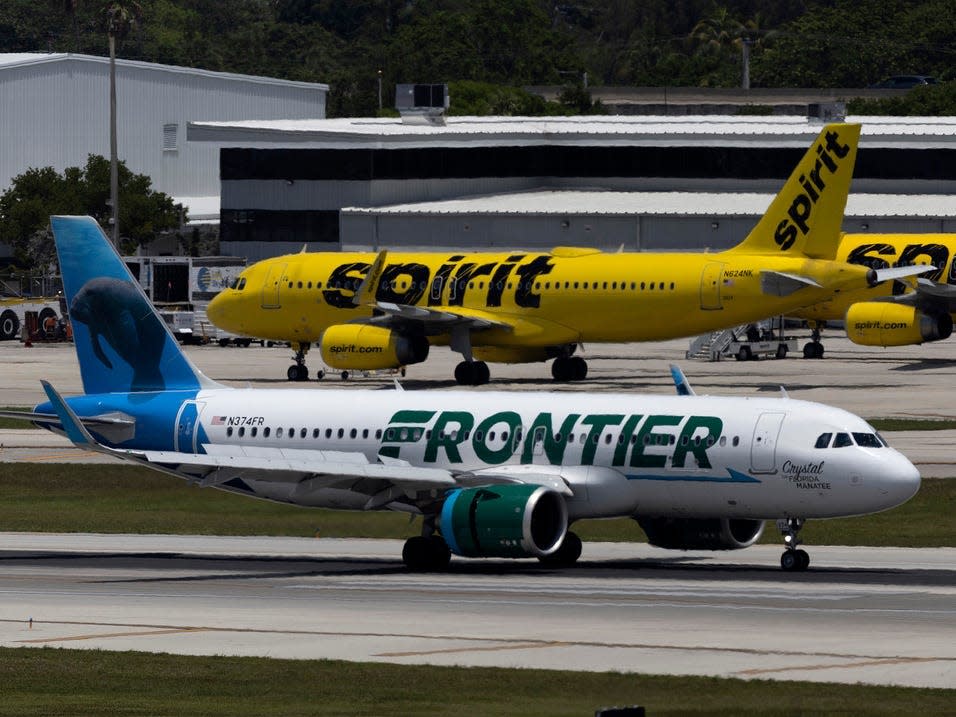 A Spirit Airlines plane behind a Frontier Airlines plane at an airport.
