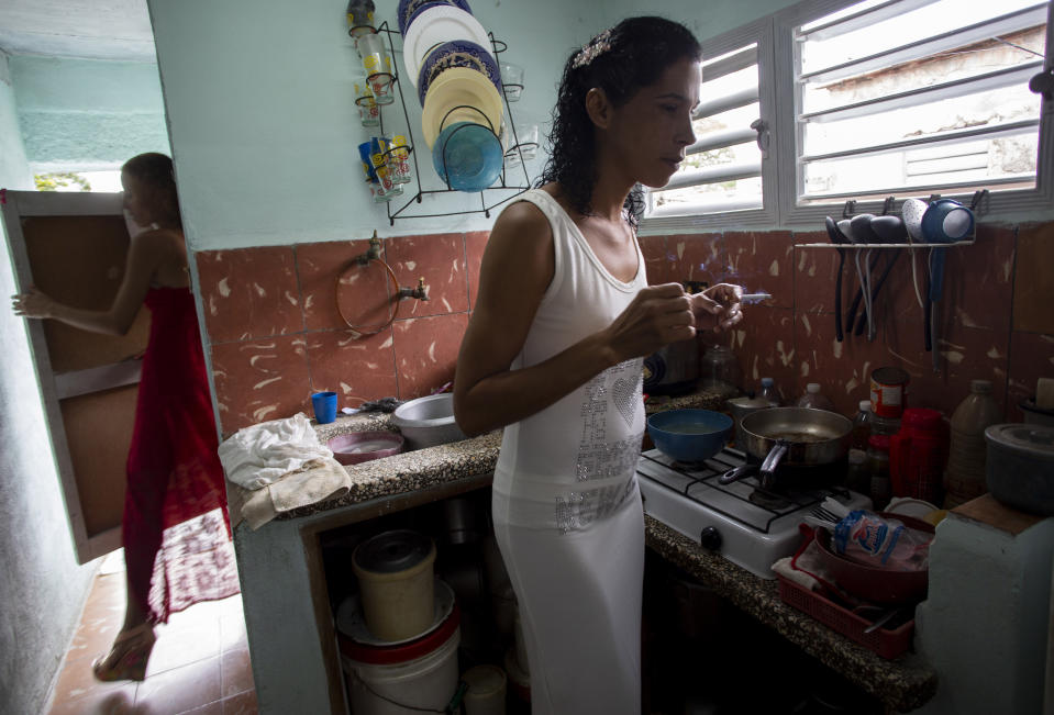 Liusba Grajales smokes in the kitchen as her fiancee Lisset Diaz Vallejo exits the bathroom, before they leave for the notary office to get married in Santa Clara, Cuba, Friday, Oct. 21, 2022. The couple, which has been together for seven years, is one of the first to make the decision to get legally married in Cuba following the new Family Code, which opened up everything from equal marriage to surrogate mothers. (AP Photo/Ismael Francisco)