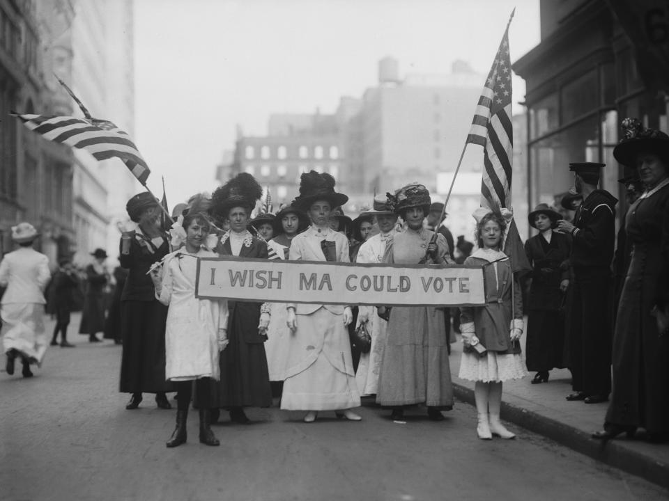 A group of suffragettes march in a parade carrying a banner circa 1913.