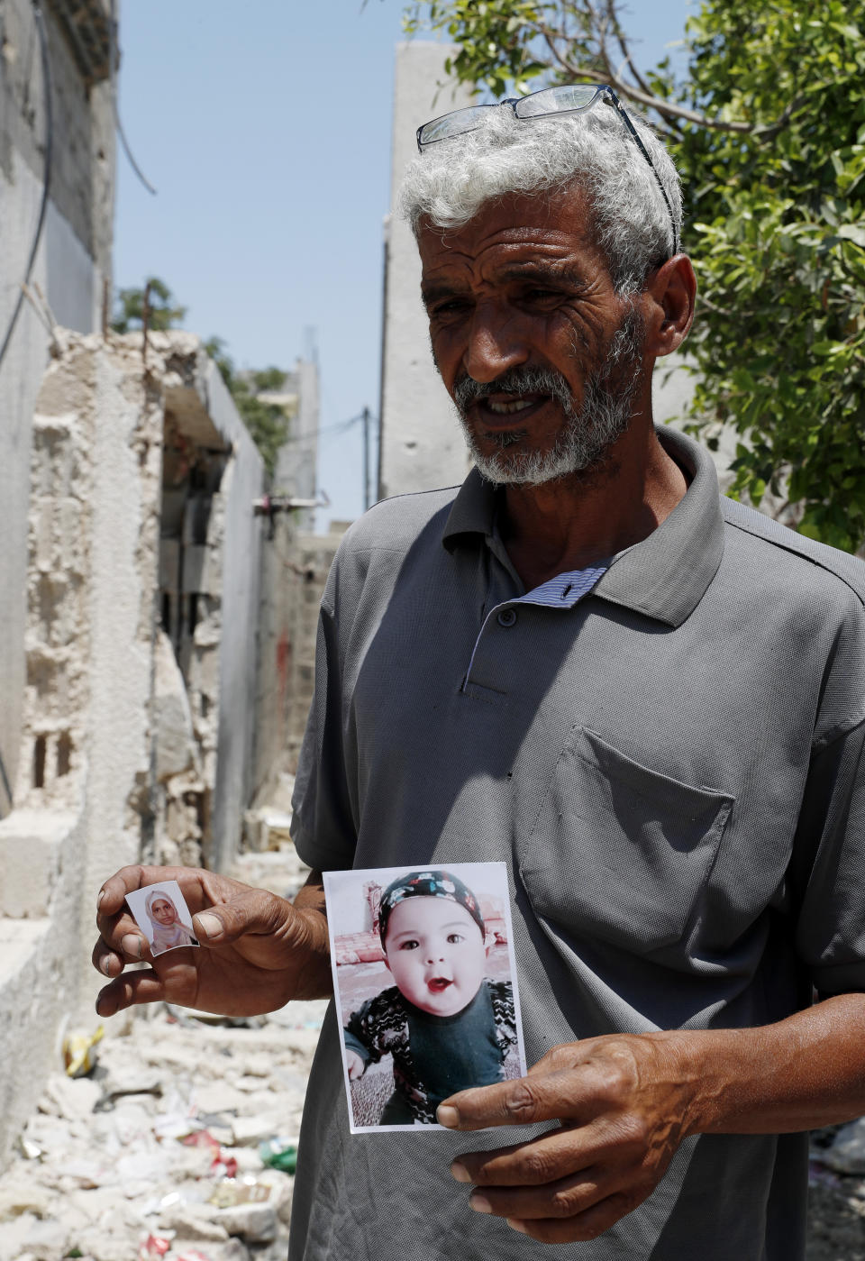 Nasser Abu Fares, who lost three of his daughters and his 9-month-old grandson when an Israeli artillery bombardment hit his family house during the 11-day war between Israel and Gaza's Hamas rulers in May, holds pictures of his grandson Mohammad, 9 months, and his daughter Fawziah, 17, amid the rubble of his house, at the Bedouin village of Umm Al-Nasr, outside the town of Beit Lahia, northern Gaza Strip, Wednesday, Aug. 4, 2021. After initially finding no grounds for disciplinary action, the Israeli military says it is investigating the artillery bombardment that killed six Palestinians, including an infant, in the Gaza Strip last May. (AP Photo/Adel Hana)