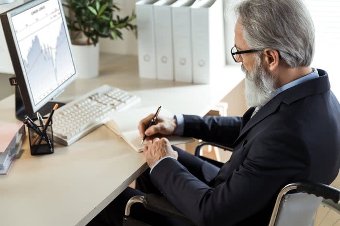 A business professional who uses a wheelchair analyzes a graph on their office computer.