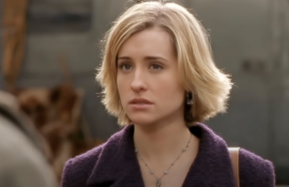 I don't know who this is. A person with short hair is looking slightly worried, wearing a coat and a necklace. The background is out of focus